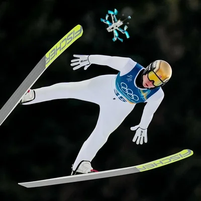 Sauteur à ski en l'air avec dossard 35 et drone en arrière-plan