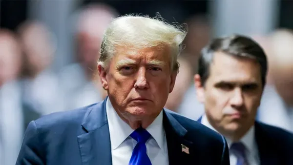 L'ancien président Donald Trump en costume bleu se tenant avec un autre homme lors d'un événement public.