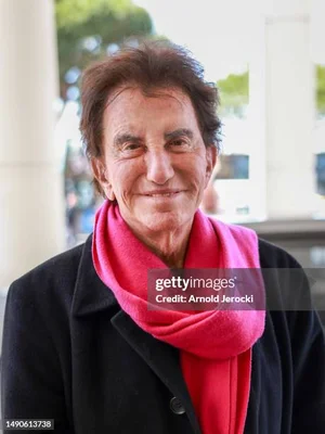 Jack Lang en extérieur portant un manteau noir et une écharpe rose.