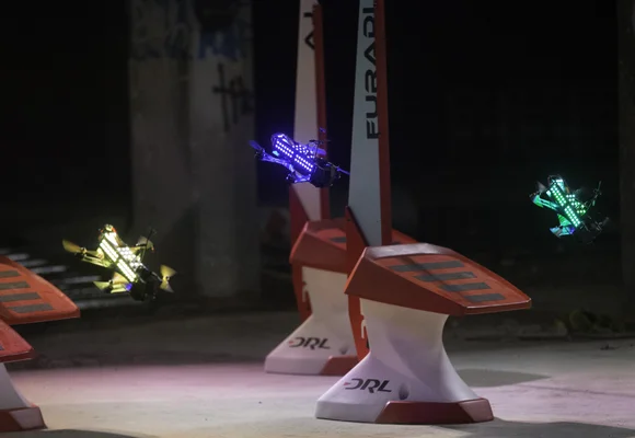 Drones DRL Racer2 illuminés volant autour d'obstacles lors d'un événement nocturne.