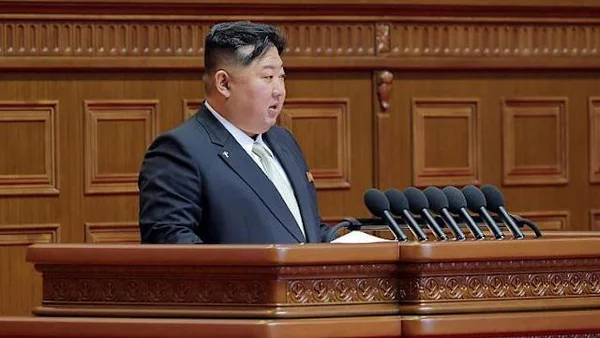 Kim Jong Un stands at a podium with military officials and North Korean flags at a formal ceremony.