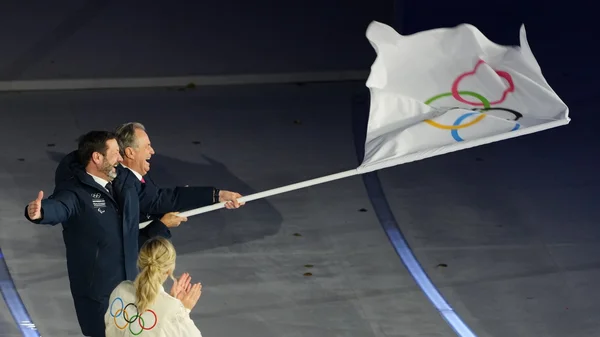 Moment protocolaire avec le drapeau olympique entouré du logo des Alpes françaises pour 2030.
