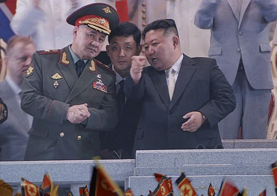 Kim Jong Un in a dark suit pointing next to a military officer