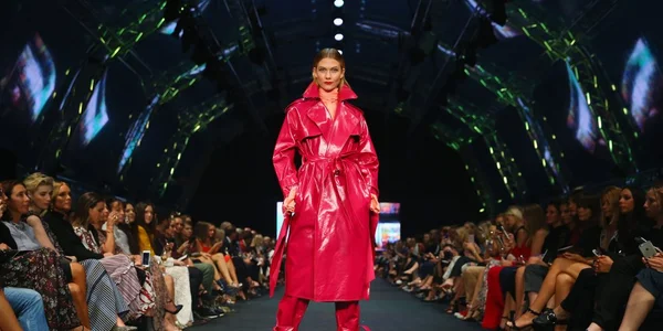 Fashion runway show with model in pink trench coat, representing Jean-Luc Brunel's modeling industry career