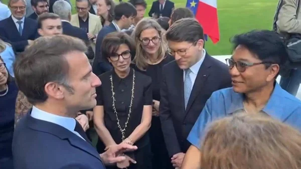 Emmanuel Macron s'adressant à un groupe lors d'un événement formel en extérieur, avec un drapeau français en arrière-plan.