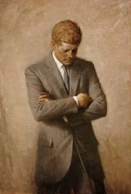 Portrait officiel posthume du président John F. Kennedy en costume gris, les bras croisés.