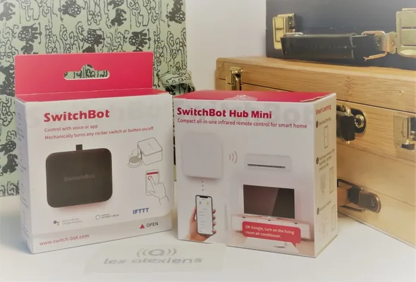 Les boîtes du SwitchBot Hub Mini et d'un Bouton SwitchBot posées sur une surface.
