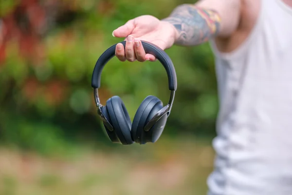 Une main tenant un casque audio noir en extérieur.