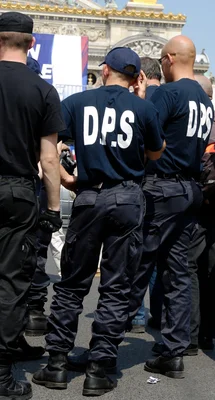 Membres du DPS surveillant la fin du cortège annuel du Front National devant un bâtiment monumental à Paris.