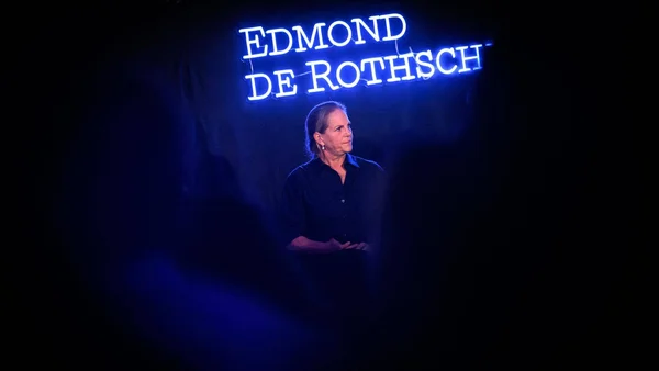 Une personne se tenant sous un enseigne lumineuse 'Edmond de Rothschild'.