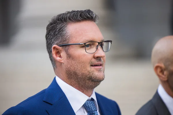 Portrait de Trevor Milton en costume bleu et lunettes.