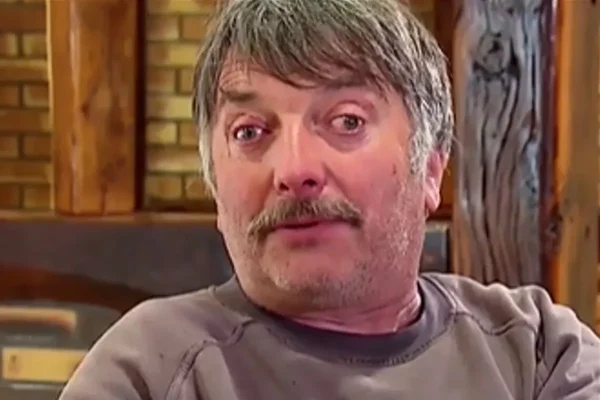 Didier posant dans un cadre intérieur avec des éléments de décoration en bois et en brique.