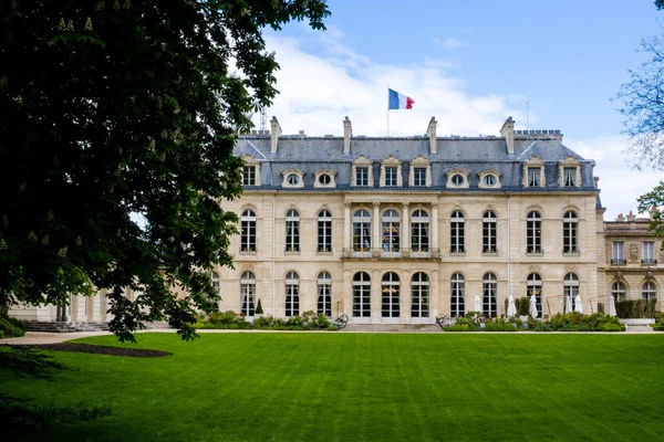 Vue du Palais de l'Élysée avec le drapeau français au sommet, devant une pelouse verte sous un ciel dégagé.