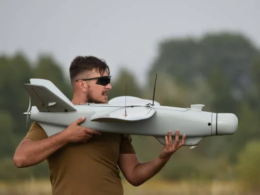 Un drone multiroute noir équipé d'une caméra volant dans un ciel bleu clair, avec des arbres flous en arrière-plan.