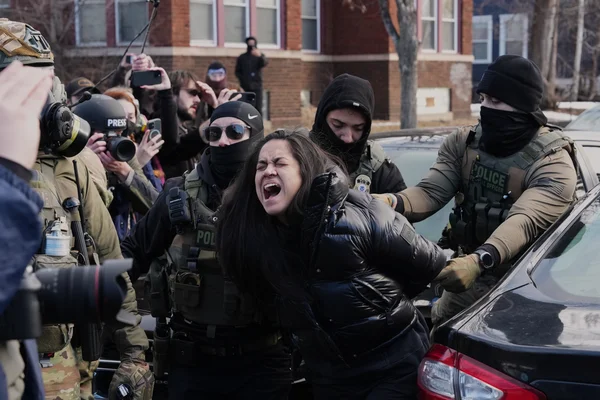 Des policiers en tenue tactique détenant une femme lors d'une intervention urbaine.