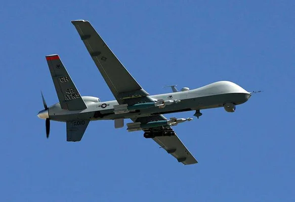 Un drone MQ-9 Reaper en vol avec ses armements sous les ailes, portant des marquages distinctifs.