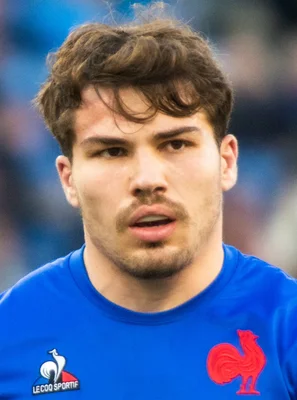 Portrait d'Antoine Dupont portant un maillot bleu à l'emblème du coq sportif.