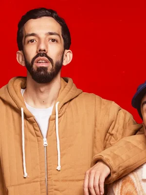 Bigflo posant seul devant un fond rouge, une personne partiellement visible à droite