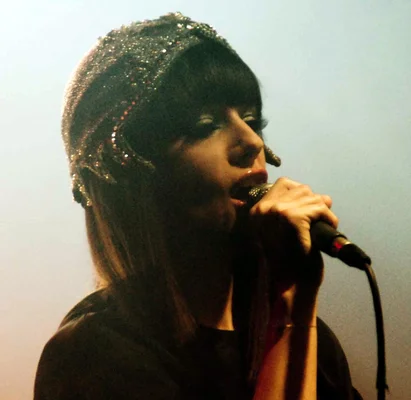 Alizée chantant, coiffée d'un couvre-chef sombre pailleté et vêtue de noir.