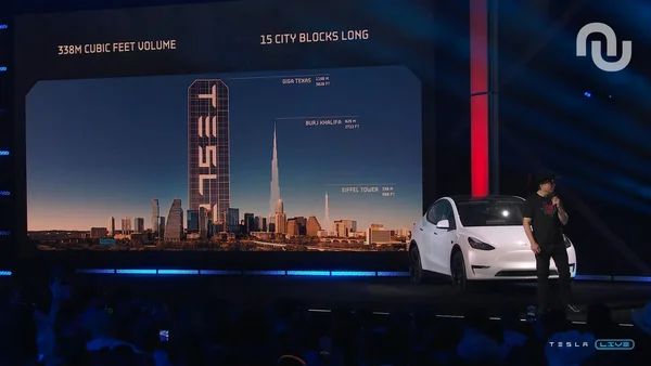 Scène lors de l'inauguration de l'usine Tesla au Texas avec un véhicule et un écran géant comparant le site à des monuments célèbres.
