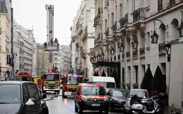 Des pompiers et leurs véhicules interviennent avec une échelle face à l'hôtel en flammes.