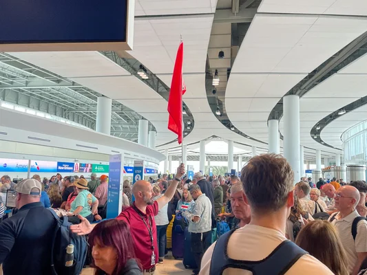 Zone d'enregistrement d'aéroport bondée avec un voyageur tenant un drapeau rouge.