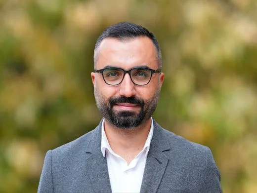 Logo DW reflété sur une vitre avec des arbres en arrière-plan.