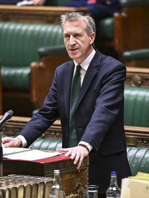 Un homme en costume et cravate verte debout devant une tribune dans une salle parlementaire.
