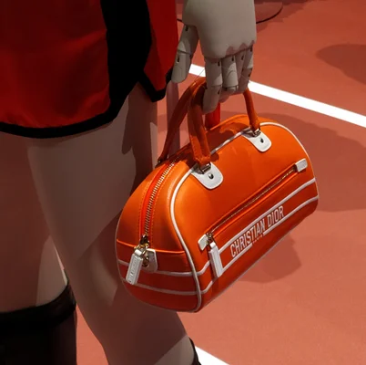 Sac à main Christian Dior orange exposé sur une main mécanique lors d'une exposition mode.