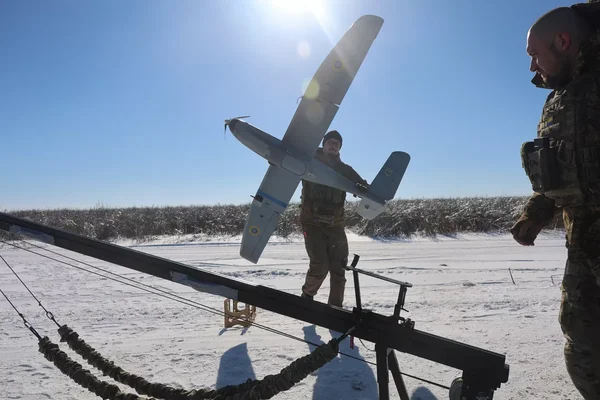 Deux militaires en tenue de camouflage dans un champ enneigé, l'un tenant un drone près d'une structure de lancement.