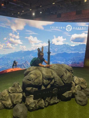 Visiteur à la Gamescom 2025 posant devant un stand Crimson Desert avec une épée dans un rocher.