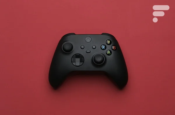 Manette Xbox noire avec boutons colorés sur fond rouge uni