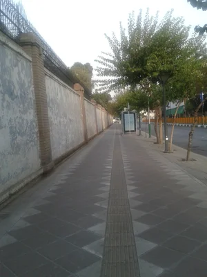 Vue d'un trottoir pavé longeant un mur de briques avec des arbres, situé près de l'ambassade du Royaume-Uni.