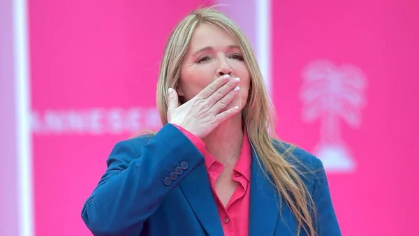 Hélène Rollès en veste bleue se cachant la bouche avec la main.