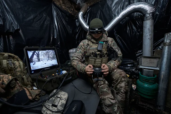 Homme en sweatshirt UKRAINE près d'un véhicule blindé et de militaires.