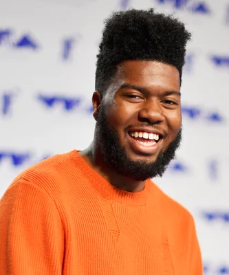 Portrait de l'artiste Khalid en pull orange, souriant face caméra.