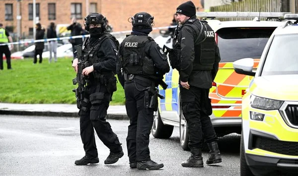 Trois agents de police en tenue tactique surveillent la zone near des barres d'immeubles à Édimbourg après l'incident.