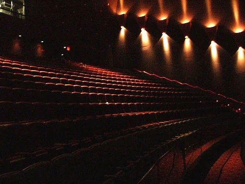 Auditorium de salle de cinéma IMAX vide avec rangées de sièges en gradins éclairés par des lumières murales.