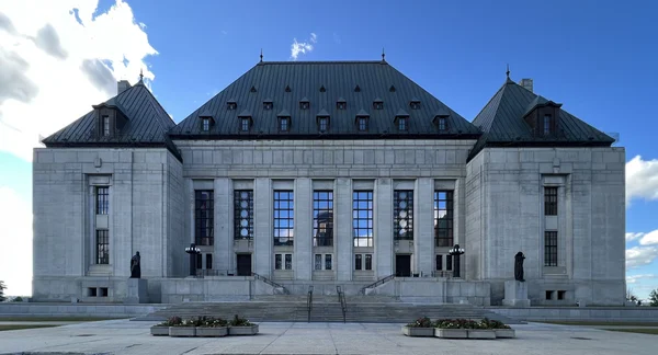 La façade de la Cour suprême du Canada, une structure en pierre symétrique avec un toit de métal sombre et de grandes colonnes.