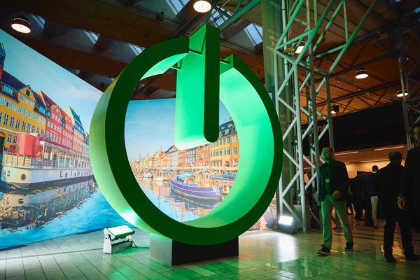 Sculpture imposante en forme de bouton d'alimentation vert exposée en intérieur, symbolisant l'engagement de Schneider Electric pour une IA plus verte.