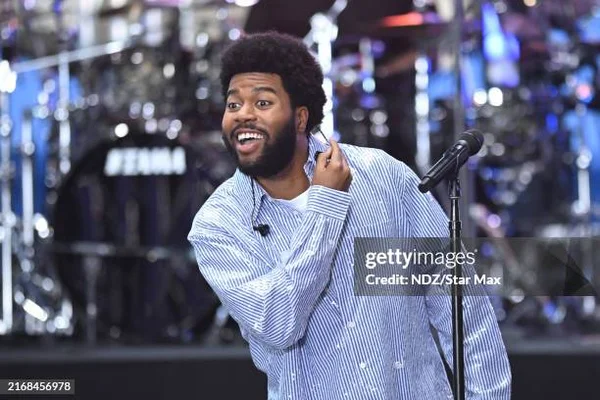Khalid chantant au micro dans une chemise bleue à rayures.