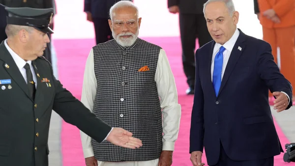 Narendra Modi posant fièrement devant un bâtiment officiel, encadré par les drapeaux de son pays.