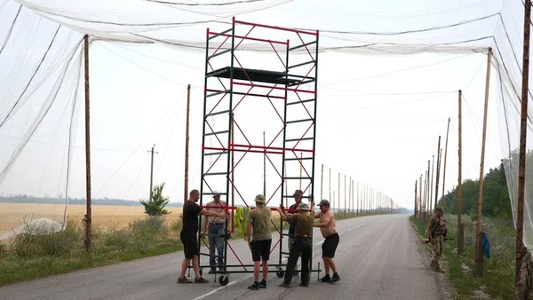 Des véhicules militaires empruntent une route couverte de filets anti-drones dans une zone boisée.