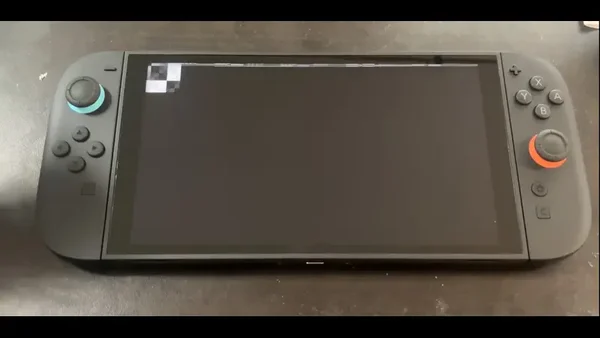 Une console Nintendo Switch en configuration portable, écran éteint et Joy-Con attachés, posée sur un fond sombre.