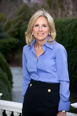 Portrait officiel de Jill Biden souriant devant un fond de verdure.