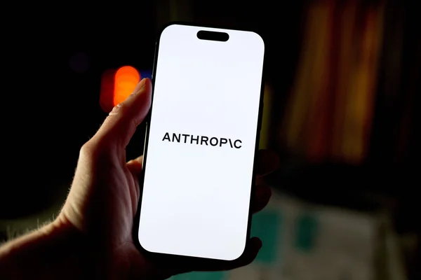 Une main tenant un smartphone affichant le texte ANTHROPIC sur fond sombre flouté