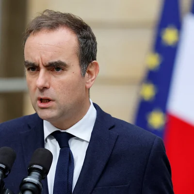 Sébastien Lecornu s'adressant à la presse depuis un podium flanqué des drapeaux français et européens.