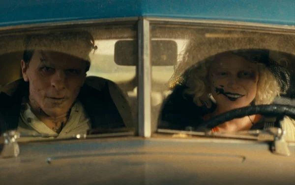 Jessie Buckley et Christian Bale vus à travers le pare-brise d'une voiture bleue.