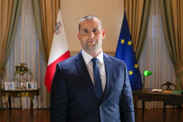Portrait officiel de Robert Abela devant les drapeaux maltais et européen.