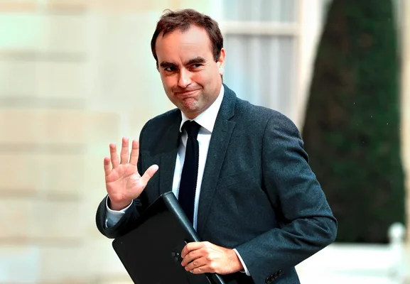 Sébastien Lecornu tenant un dossier et saluant de la main.